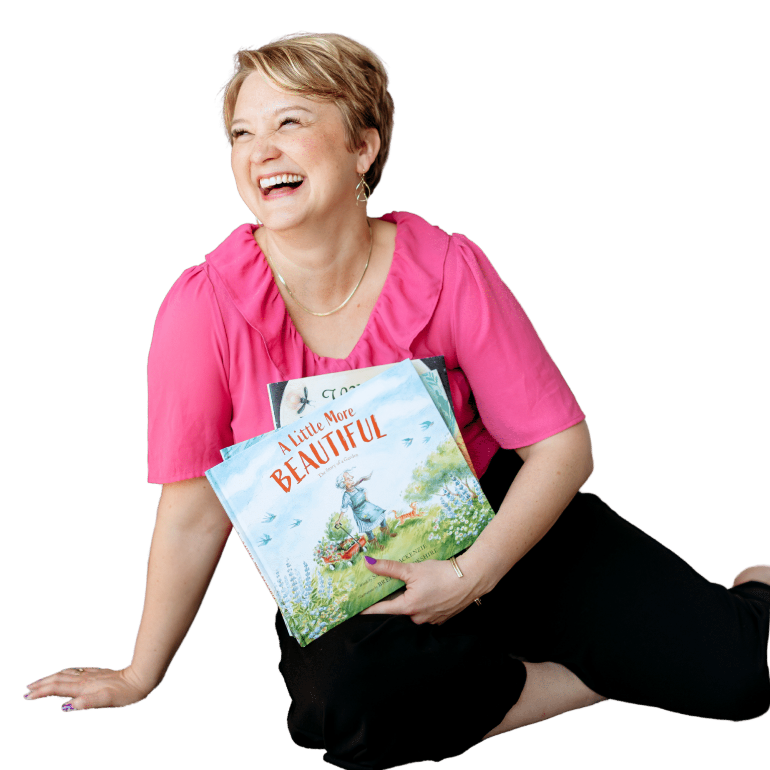 Smiling woman with short blond hair in a pink blouse, holding colorful books against a black background.