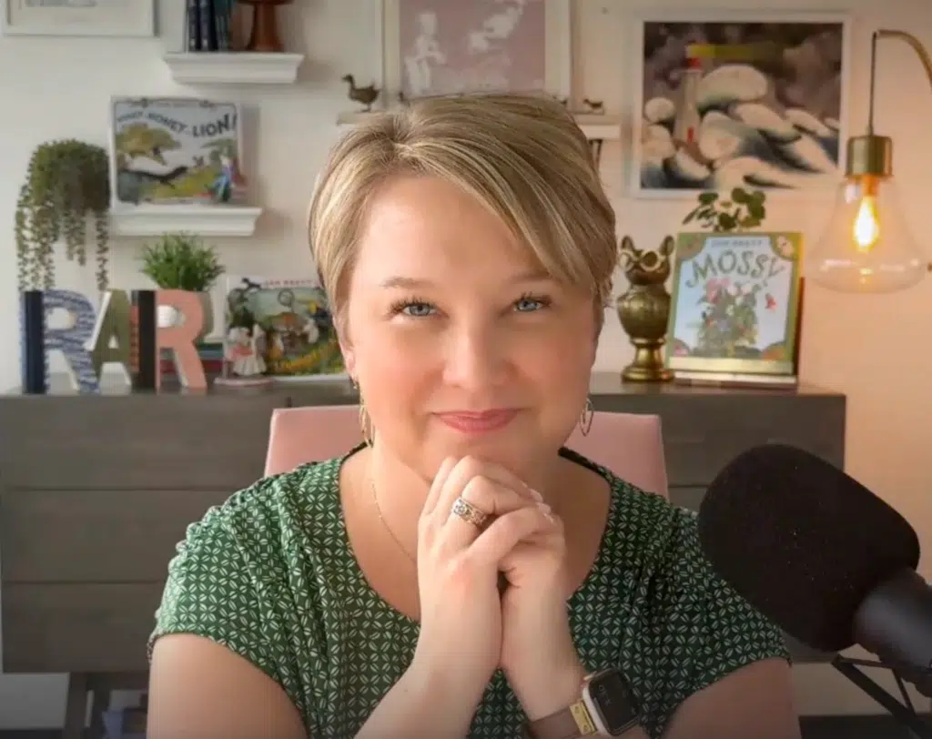 Screenshot 2026-04-30 at 51830 PM - Read-Aloud Revival ® with Sarah Mackenzie Close-up of a smiling woman with short blonde hair in a green patterned blouse in a cozy, book-filled room with plants and warm lighting behind her
