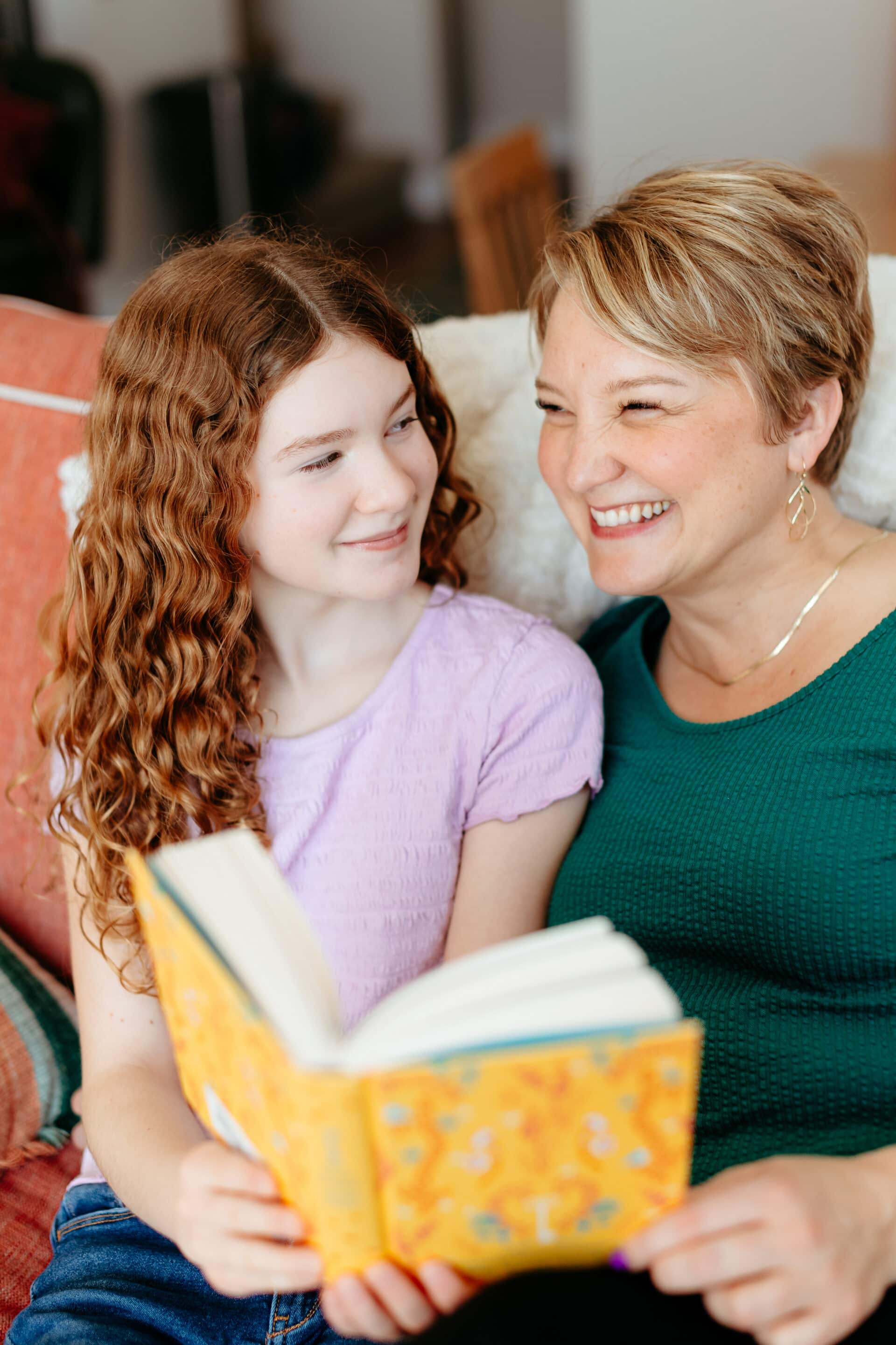 Smiling woman and girl reading a colorful book together on a couch.