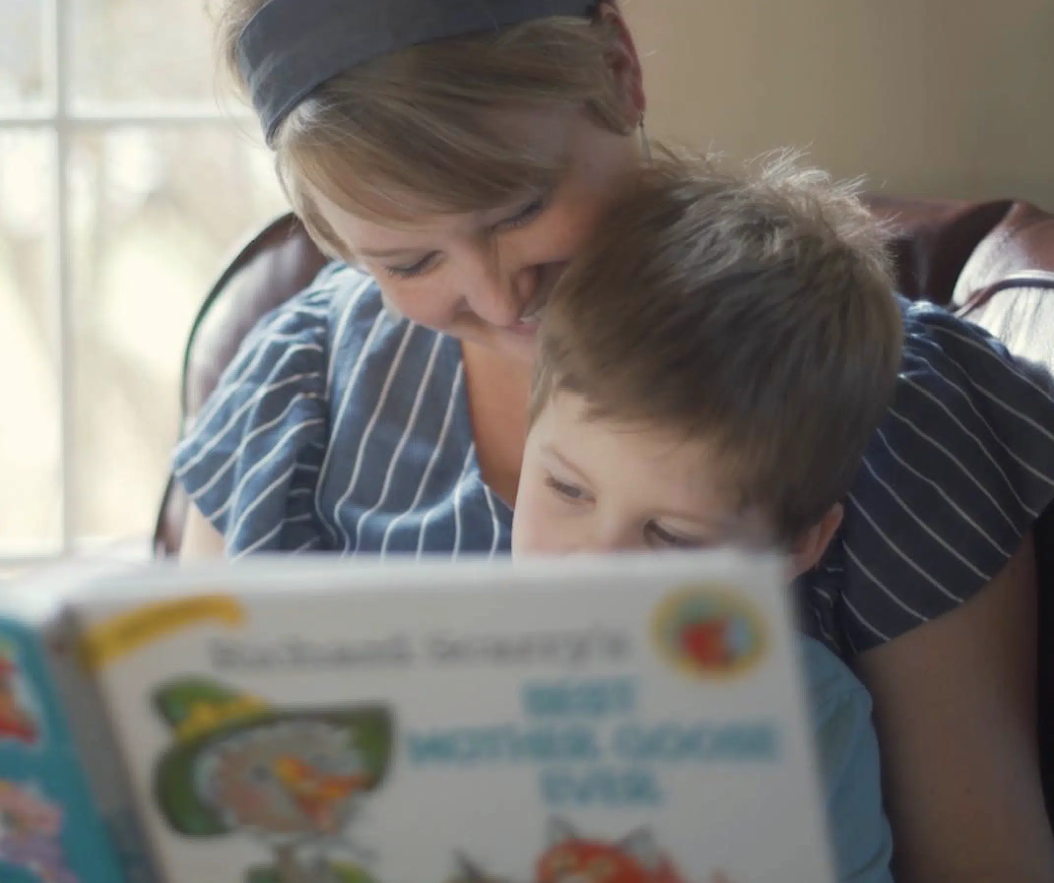 Woman and young child reading a colorful children's book together indoors, smiling.