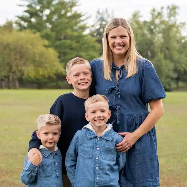 Emily-Hines - Read-Aloud Revival ® with Sarah Mackenzie Mother posing with her four sons in a grassy park, all smiling at the camera.