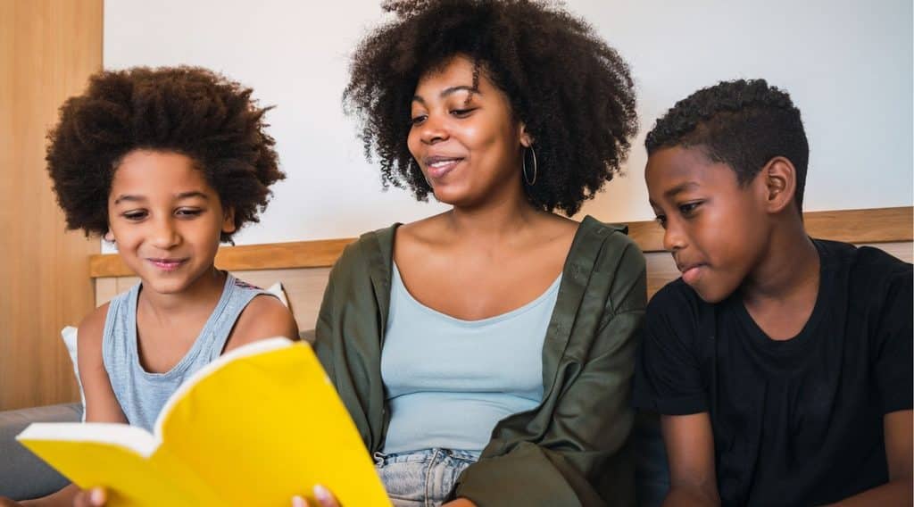 Mother and two kids reading a bright yellow book together on a sofa indoors.